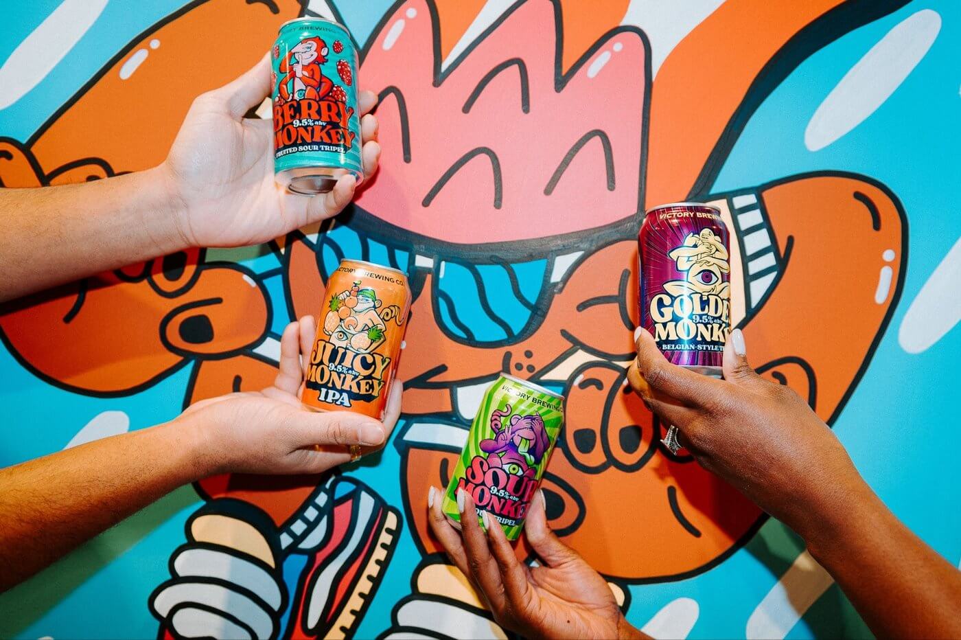 Hands holding different cans of Victory Brewing Monkey Beers